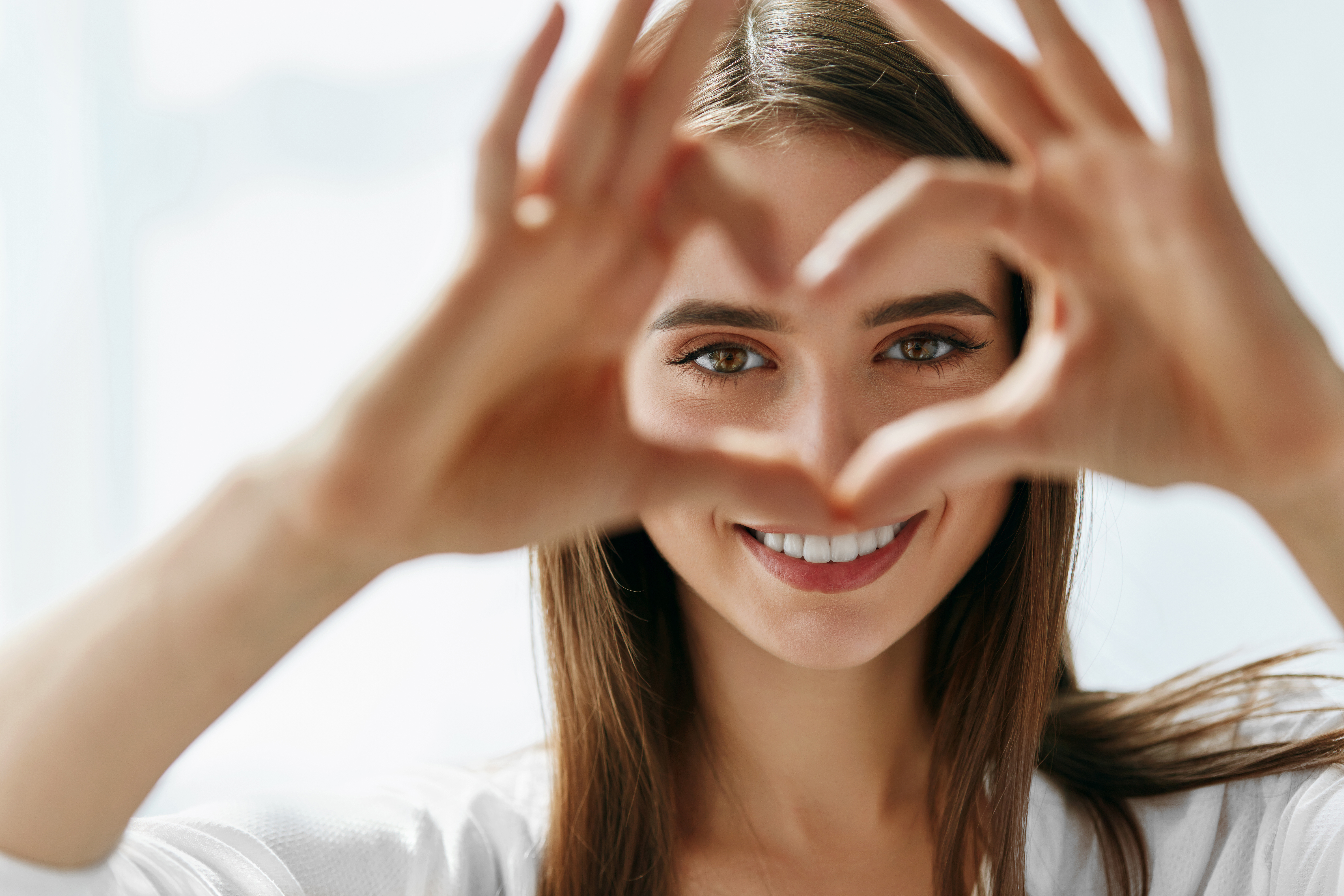 Smiling girl with bright white teeth making a heart shape with her hands