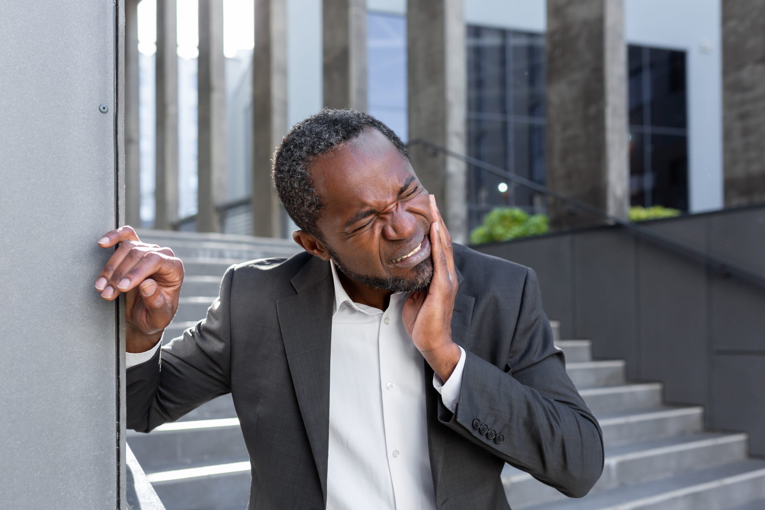 man in a suit holding his jaw indicating severe tooth pain, possible dental emergency 