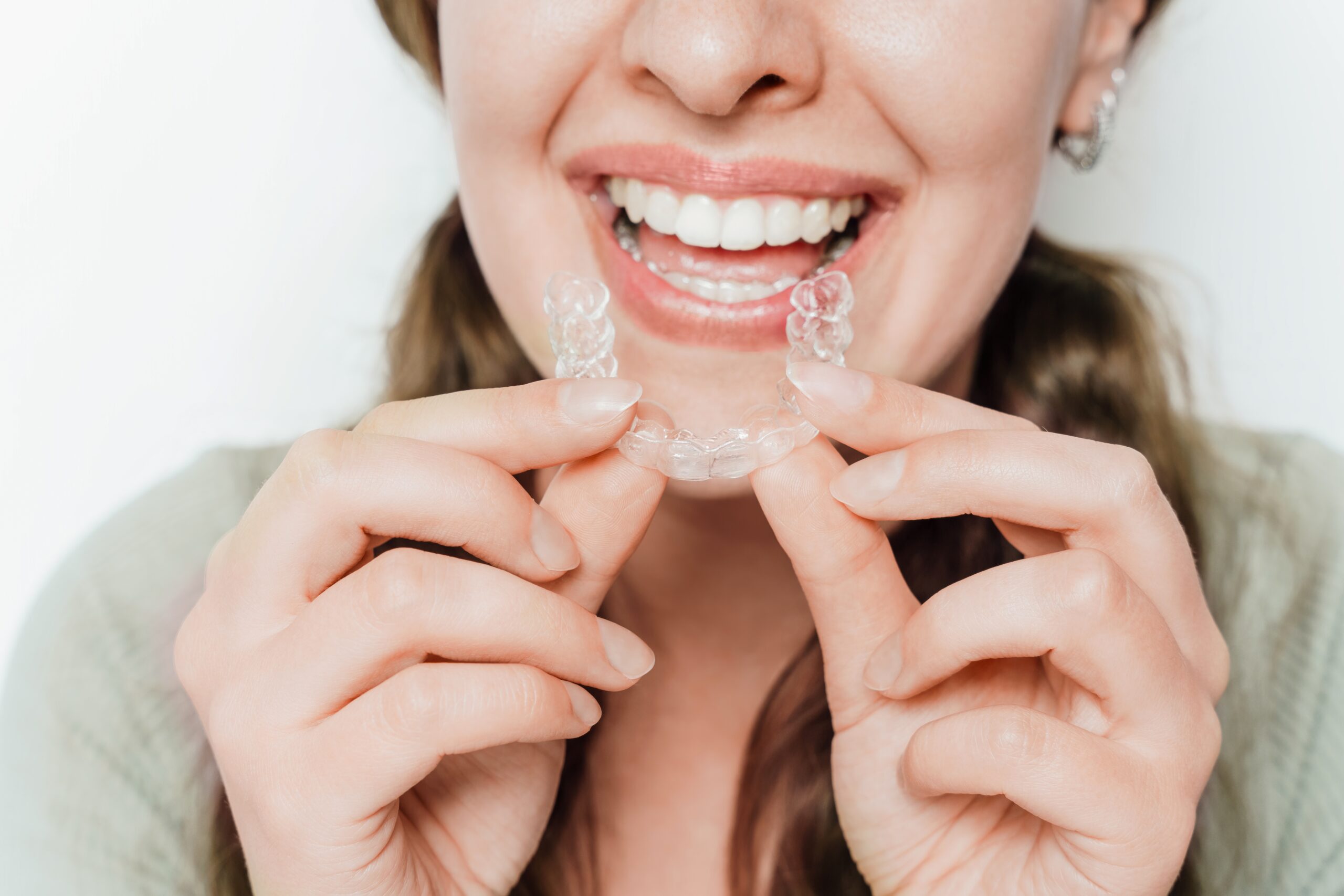 smiling young woman putting in her clear aligners against a white background