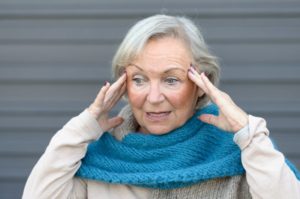 Elderly woman with her hands to her temples in confusion