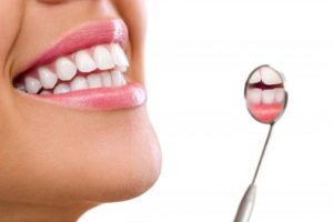 Smiling woman with teeth reflected in inspection mirror